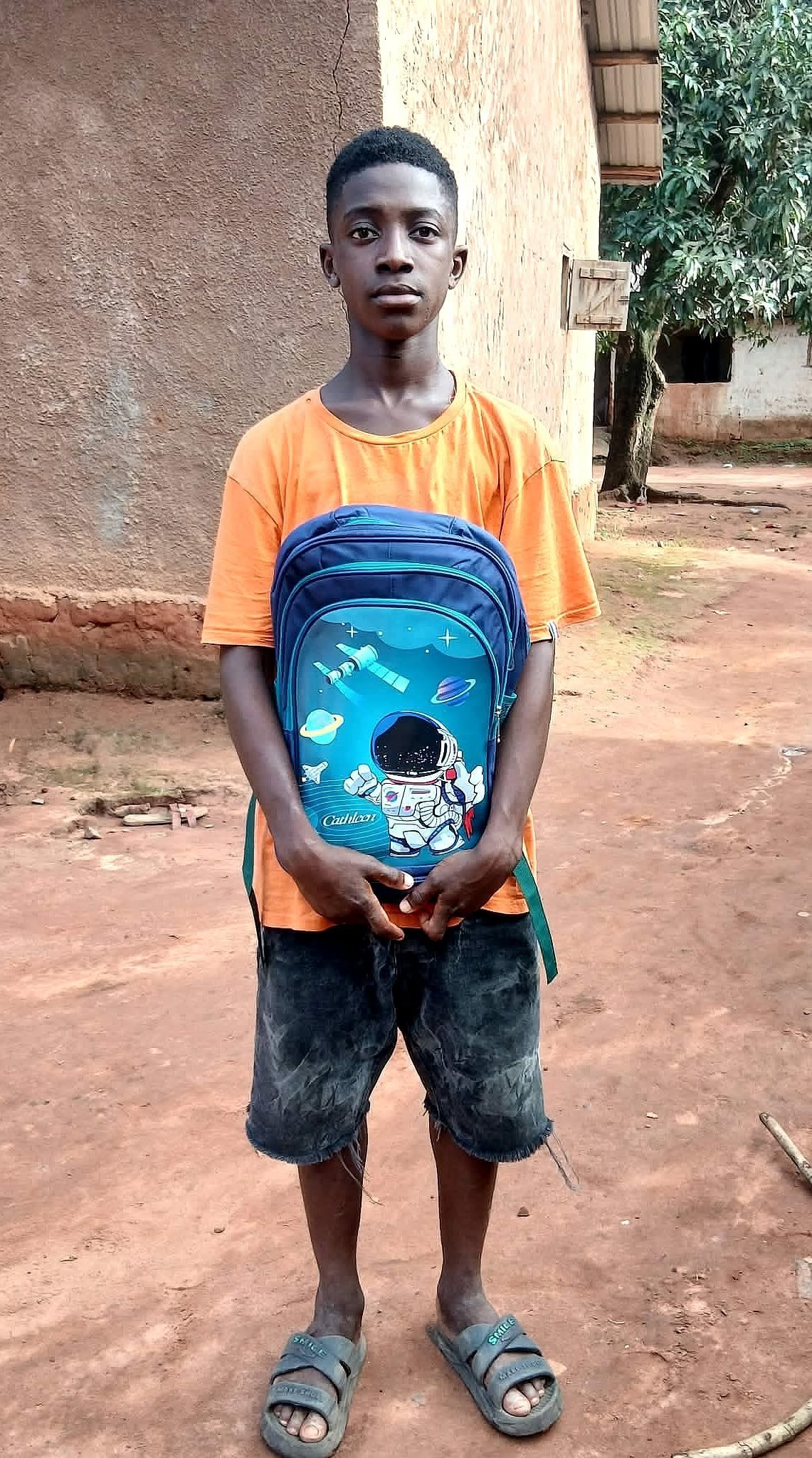Escolar con camiseta naranja sosteniendo una mochila azul